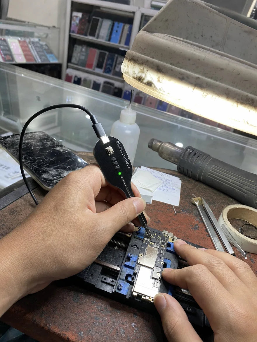 Customer photo: CircuitSense probe on a smartphone motherboard at a repair shop counter